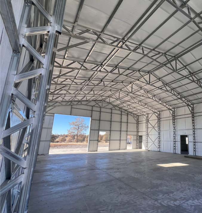 Large industrial-grade clear-span metal barns structure with a lean-to side shed, perfect for heavy farm machinery and feed storage.